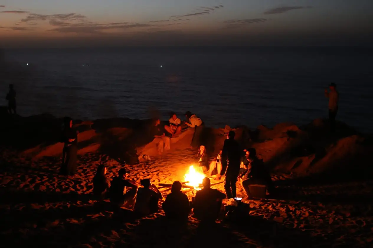 Hoguera en la playa de noche con el grupo sentado alrededor