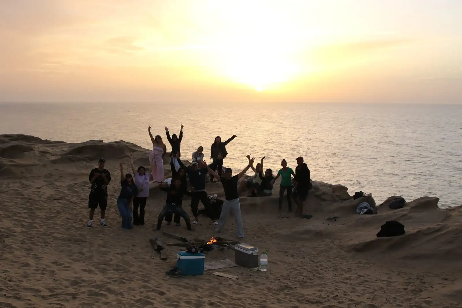 Atardecer sobre el océano desde las dunas, con el grupo celebrando en la arena